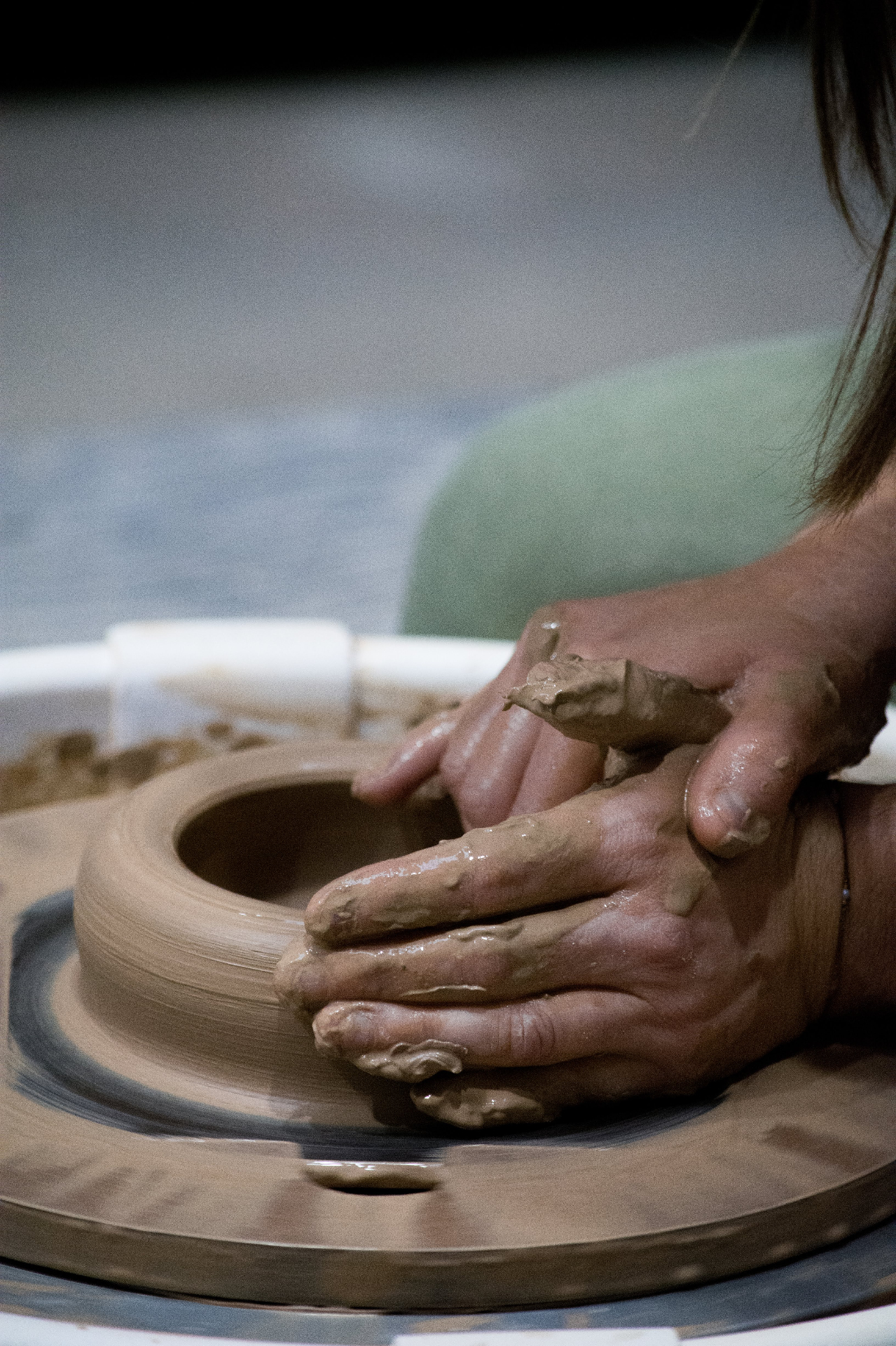 Close view of clay-covered hands shaping a wheel-thrown vessel in the Muds studio